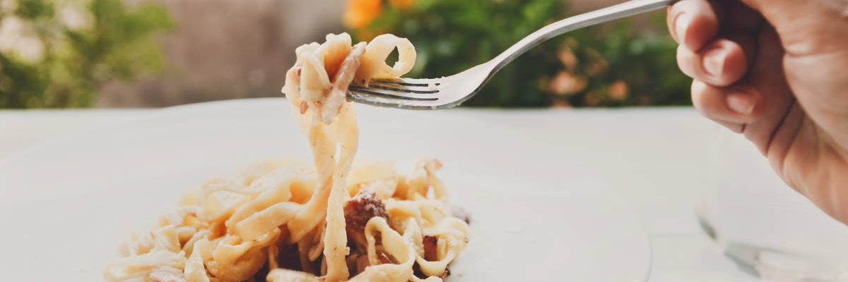 ristoranti a saturnia terme Eating pasta. Fork closeup. Traditional italian carbonara with bacon, egg and parmesan decorated with basil on white round plate at wooden table. Restaurant food, selective focus